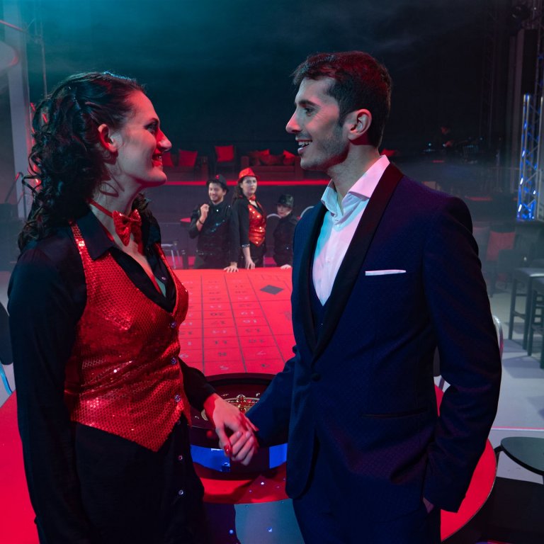 Violetta und Alfredo, im Hintergrund beobachten sie Flora und Croupier