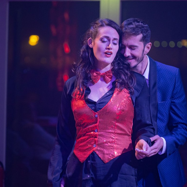 Alfredo steht hinter Violetta und hält ihre Hand